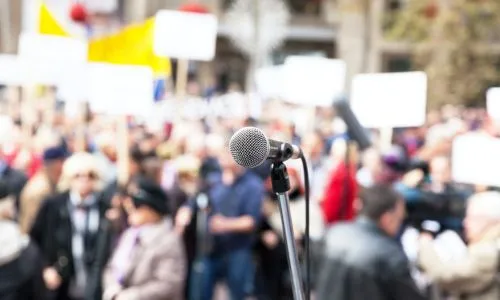 Au 1er plan, un micro, au second, des gens qui manifestent dans la rue.