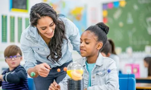 Une jeune femme aide une élève, en classe.