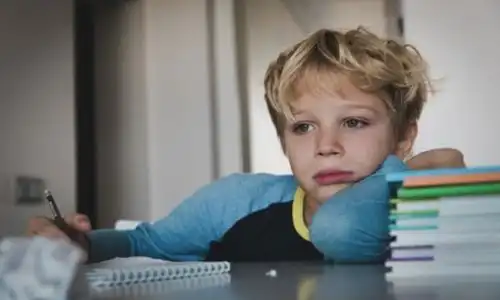 Un enfant l’air triste, qui s’appuie sur une pile de livre.