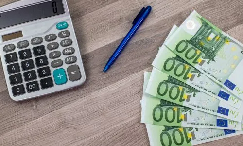 Des billets de 100 euros étalés près d’une calculatrice et d’un stylo.