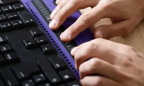 Zoom sur les mains d’un homme aveugle qui tape sur son clavier numérique adapté.