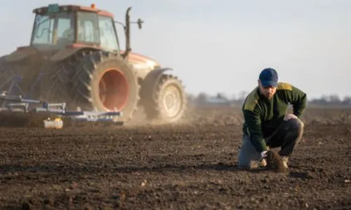 Un agriculteur en train d’examiner la terre devant un tracteur.