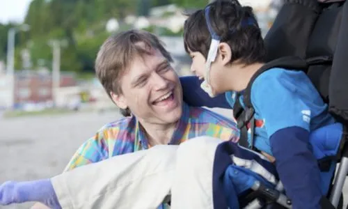 Un père et son fils en fauteuil roulant en train de rigoler dans la rue.