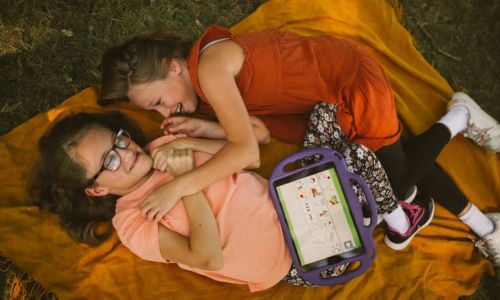 2 fillettes, allongées dans l’herbe, rient. L’une d’elles tient son carnet MCPV.