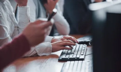 Zoom sur des mains qui tapent sur un clavier d’ordinateur, à côté d’autres gens