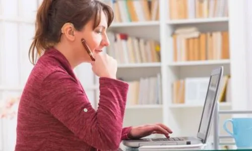 Une femme, de profil, munie d’un appareil auditif pianote sur son ordinateur.