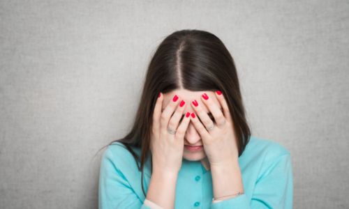 Jeune femme brune couvrant son visage avec ses deux mains.