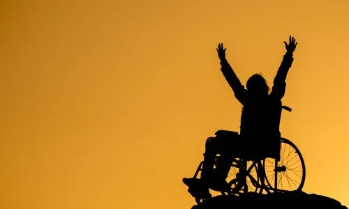 L’ombre d’une personne en fauteuil roulant levant les bras en l’air.