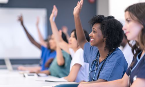 Des étudiants en médecine, en classe, lèvent la main.