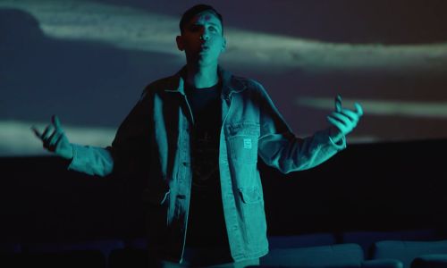 Guillaume Muller face caméra dans son clip, devant un écran de cinéma.