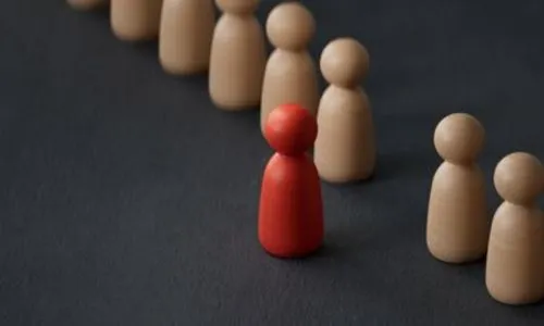 Une figurine en bois rouge se détache d’un groupe de figurines en bois beige.