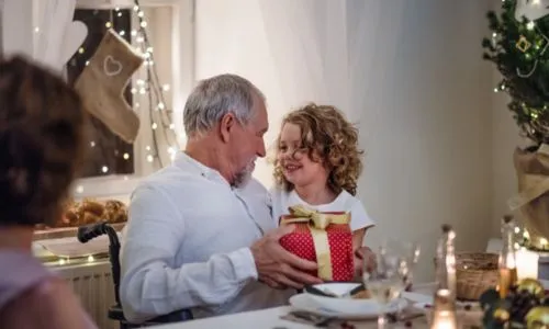 Un grand-père en fauteuil roulant tient un cadeau en regardant sa petite fille.