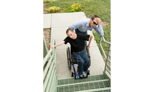 Un homme en fauteuil roulant et son accompagnant désabusés face à un escalier.