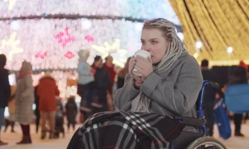 Une jeune femme en fauteuil roulant boit un café sur un marché de Noël.