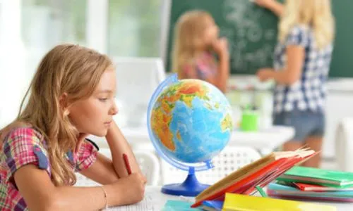 Une jeune fille regarde un globe derrière une enseignante avec une autre élève.