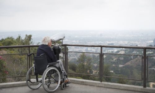 Un homme âgé en fauteuil roulant regarde la ville à travers des jumelles.