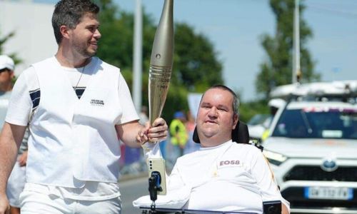 Matthieu Travers porte la flamme olympique, vêtu de blanc.