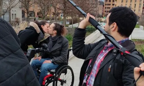 Un comédien en fauteuil roulant et une femme s’embrassent lors d’un tournage.