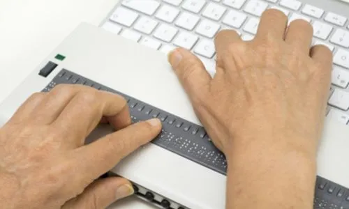 Zoom sur les mains d’un homme pianotant sur un clavier adapté aux aveugles.