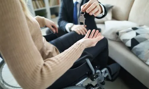 Un homme donne les clés d’une maison à une femme en fauteuil roulant.