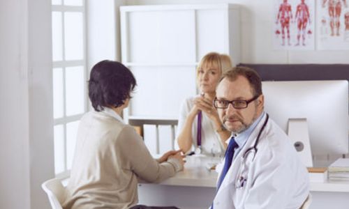 Un médecin regardant l’objectif avec un patient en arrière-plan