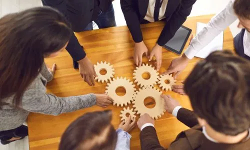 Plusieurs personnes en costume dépose des rouages sur une table.