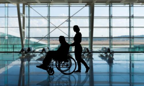 Silhouette d'une femme poussant une personne en fauteuil roulant à l'aéroport.