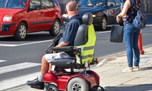 Un homme en fauteuil roulant attend pour traverser au passage piéton, en ville.