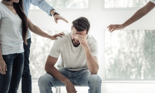 Un groupe de personnes touche un homme assis sur une chaise, la mine triste.