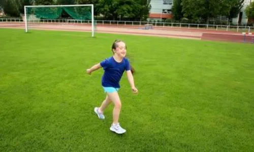 Une jeune fille avec trisomie court sur un terrain de foot.