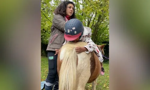 Une petite fille monte un cheval accompagnée par une médiatrice animalière.