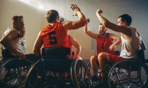 Des joueurs de rugby à XIII fauteuil, en cercle, lèvent le bras.
