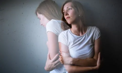 Une femme pensive, la mine triste, les bras croisés, qui se dédouble.