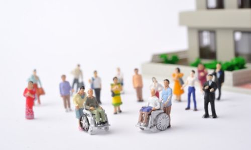 Des petites figurines, dont certaines en fauteuil roulant, devant un bâtiment.