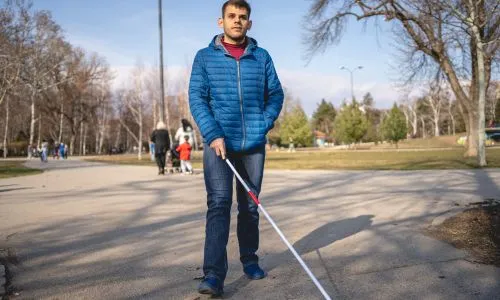 Un homme aveugle marche dans un parc avec sa canne blanche.