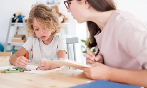 Un enfant dessine à côté d’une femme qui prend des notes.